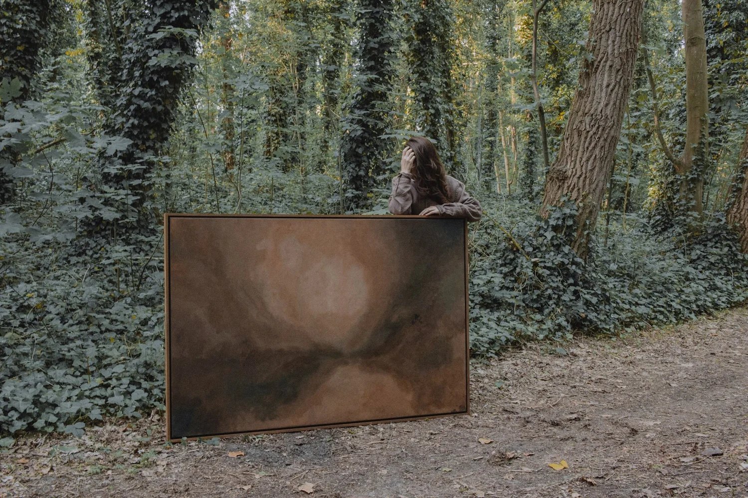 A painting by Raluca Luchian stood up on the forest floor, the artist behind it